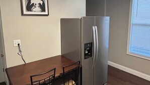 Une cuisine avec une table en bois, des chaises, un réfrigérateur et un luminaire fixé au mur.