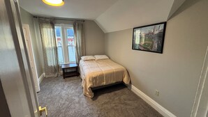 Une chambre à coucher avec un lit, une table de chevet, une fenêtre avec des rideaux et un tableau encadré au mur.