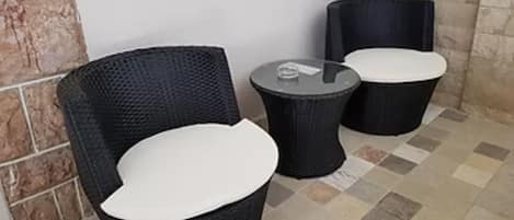 A corner with a wicker chair and a small round table with a white cushion.