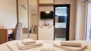 A hotel room with a bed, a flat-screen TV, a mirror, a wardrobe, and a bathroom visible through an open door.