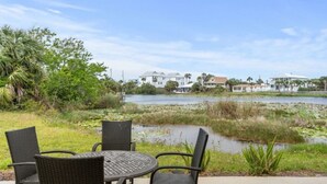 Un patio con sillas de mimbre y una mesa con vista a un cuerpo de agua y casas al fondo.