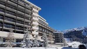 Ein mehrstöckiges Hotel mit Balkonen, schneebedeckten Bäumen und einer Bergkulisse.