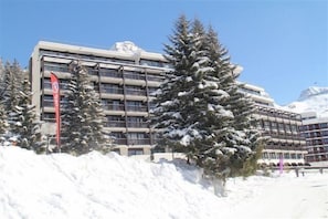 Ein mehrstöckiges Hotel mit modernem architektonischen Design, umgeben von schneebedeckten Bäumen und einem klaren Himmel.