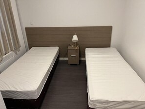 Ein kleines Hotelzimmer mit zwei Einzelbetten, einem Holzkopfteil, einem Nachttisch mit Lampe und einem Heizkörper.