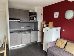 Eine kompakte Küche mit Mikrowelle, Herd und Kühlschrank, neben einem Sitzbereich mit einer Couch und Kissen.