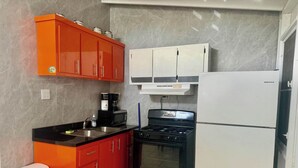 Een compacte keuken met een gasfornuis, een magnetron, een spoelbak en een koelkast.