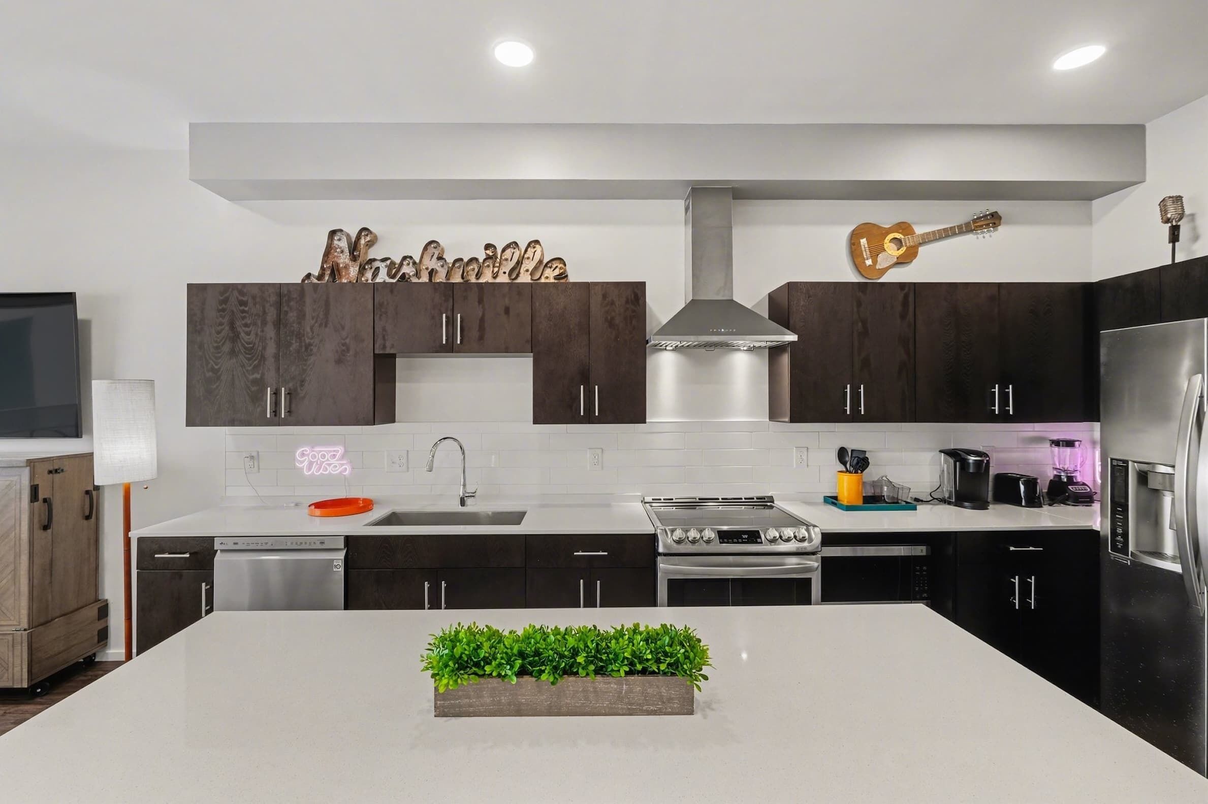 Een moderne keuken met donkere kastjes, een centraal eiland met een plant, en een gitaar aan de wand.