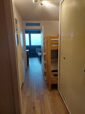 Ein schmales Gang mit einem Etagenbett, einem Kleiderschrank und einem Fenster mit Blick.