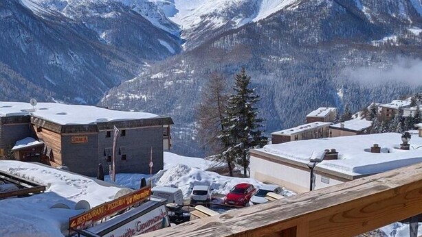 Vista de la montaña con balcón de madera, un restaurante y paisaje nevado.