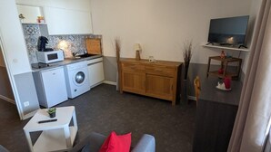 Un espacio habitable compacto con kitchenette, lavadora, comedor con televisor y sofá.