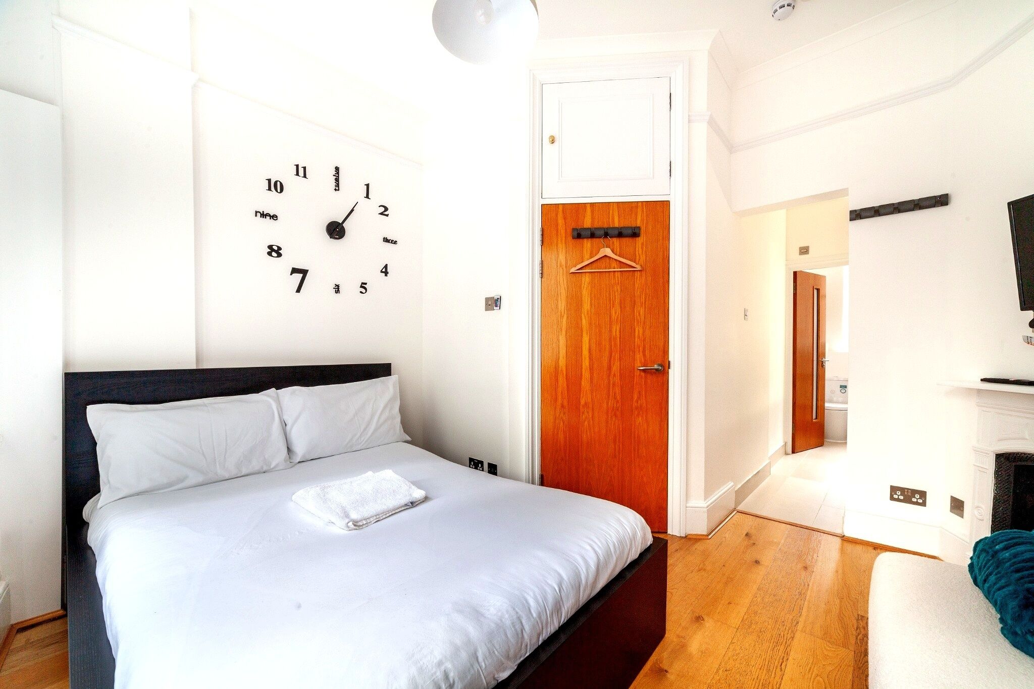 Ein Schlafzimmer mit einem Bett, einer Wanduhr, einer Holztür und einem Flur, der zu einem Badezimmer führt.