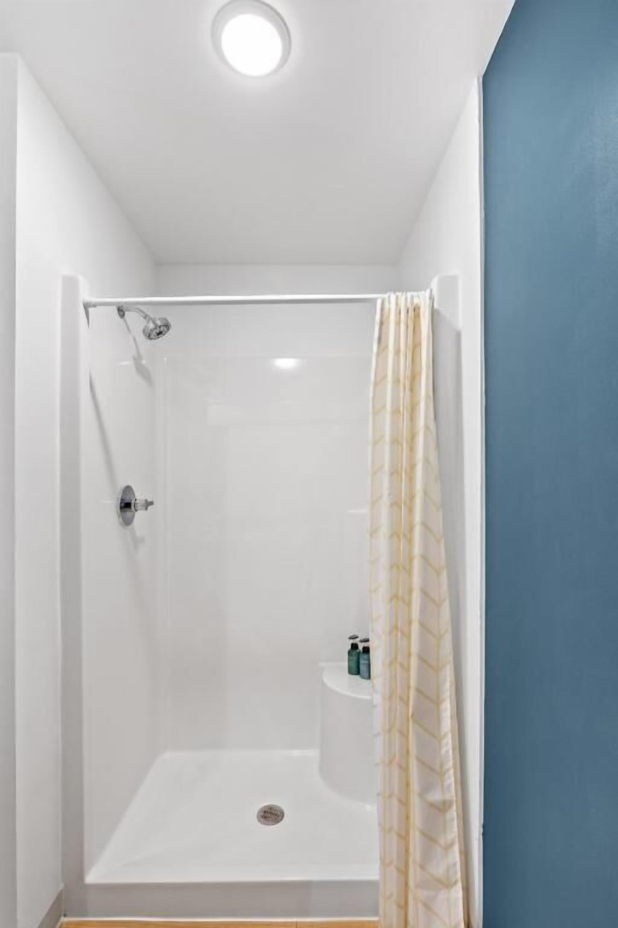 Una ducha a ras de suelo con puerta de cristal, un cabezal de ducha y un estante pequeño con artículos de aseo.