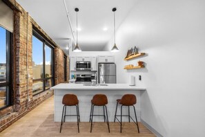 A modern kitchen with white cabinets, a central island with bar stools, and pendant lighting. - Enger Lofts Hotel & Marketplace (Duluth)