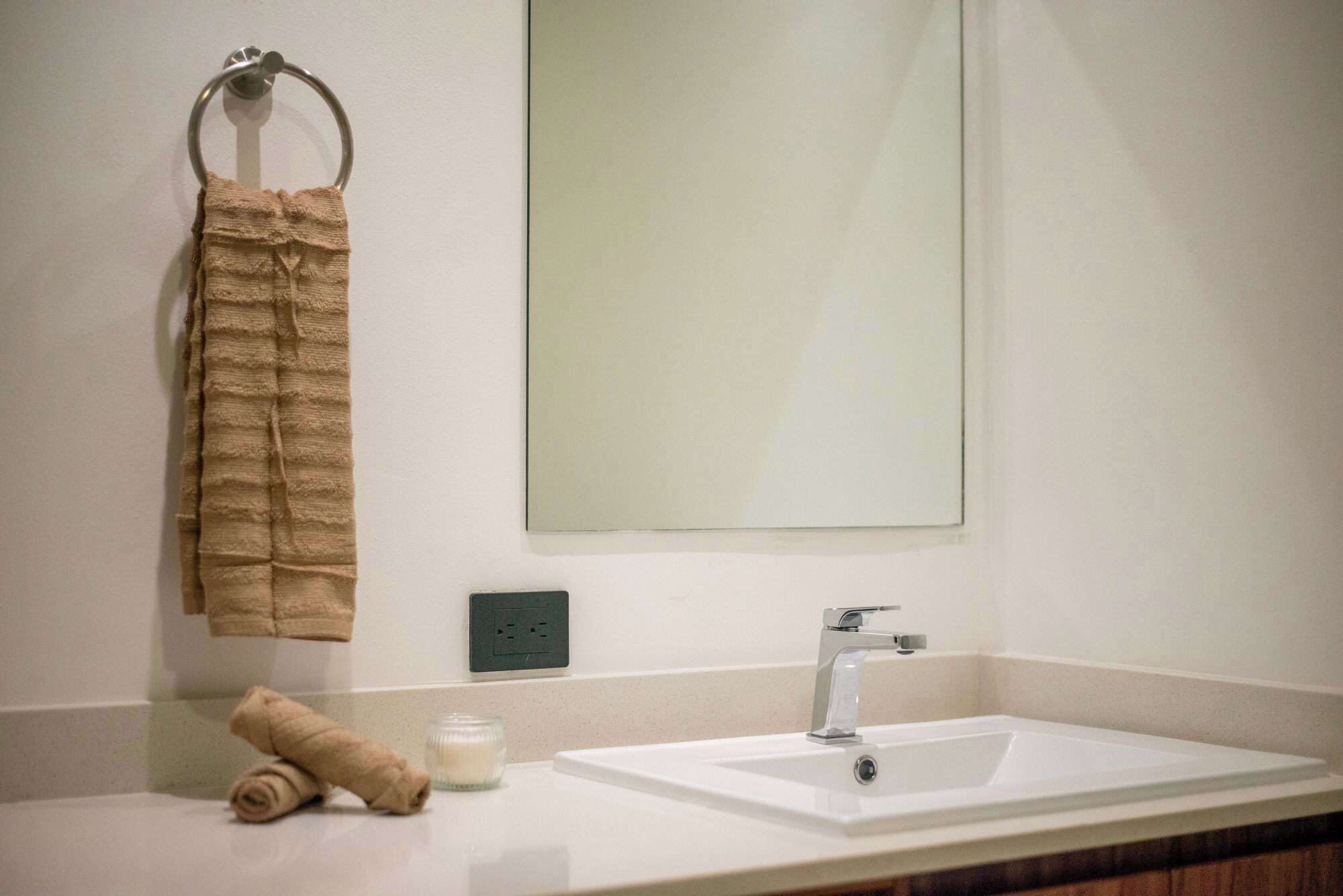 A bathroom with a sink, mirror, towel rack, and a rolled towel on the counter.