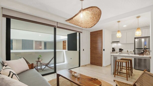 A modern living room with a sofa, coffee table, and wicker chairs. There is a kitchen with a refrigerator, stove, and bar stools. - Rooftop Pool & Gym walkable studio full equipped (Playa del Carmen)