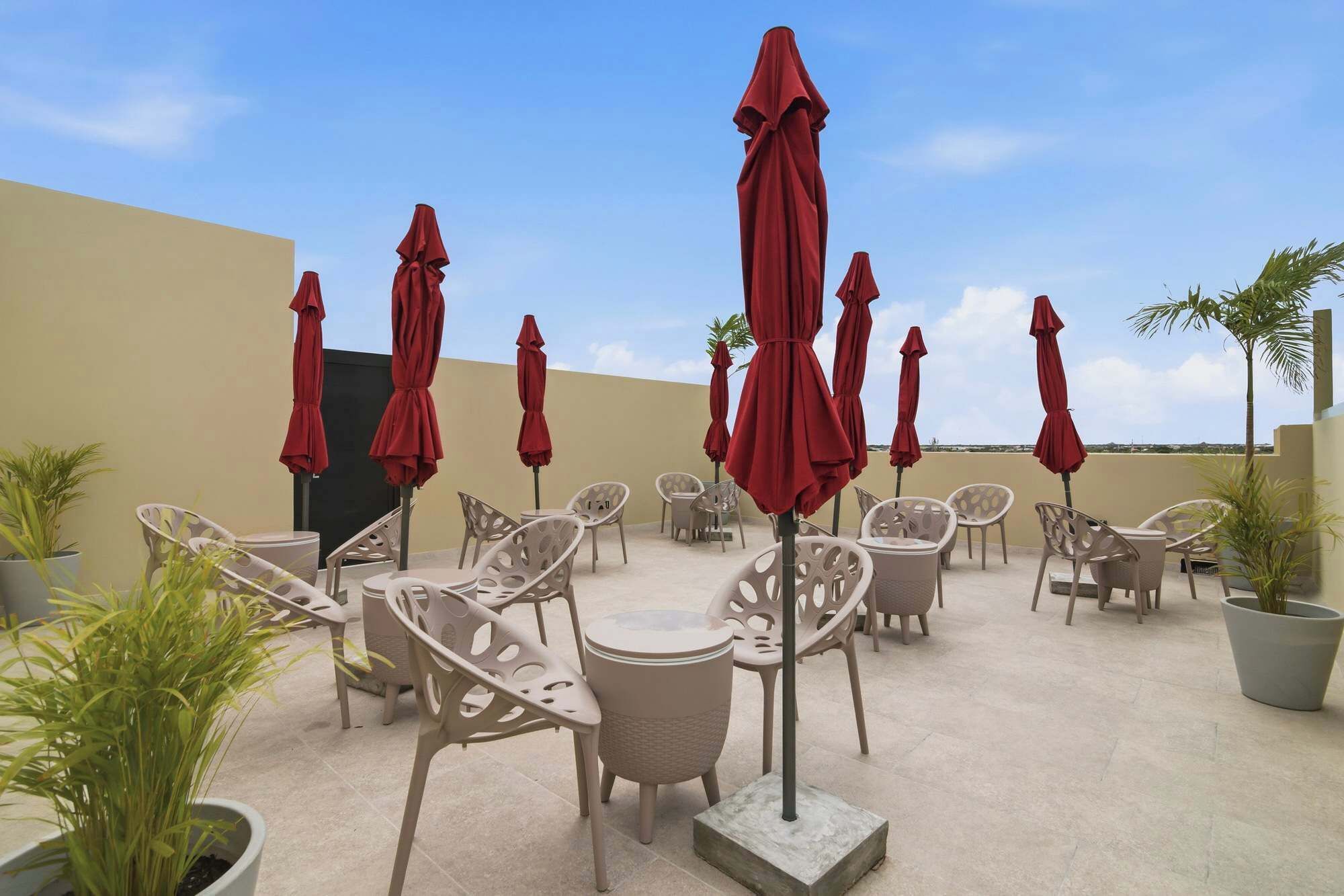 An outdoor seating area with chairs and red umbrellas, potted plants, and a clear sky.