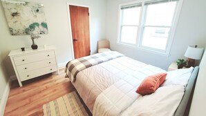 Un dormitorio con cama, cómoda, puerta, ventana y un cuadro en la pared.