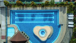 Vista aérea de una piscina con diseño en forma de corazón, rodeada por una terraza empavedada y un pequeño pabellón.