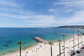 A beach with clear blue water, a rocky breakwater, and palm trees. - Beachfront Apt with Mediterranean View & Parking (Antibes)