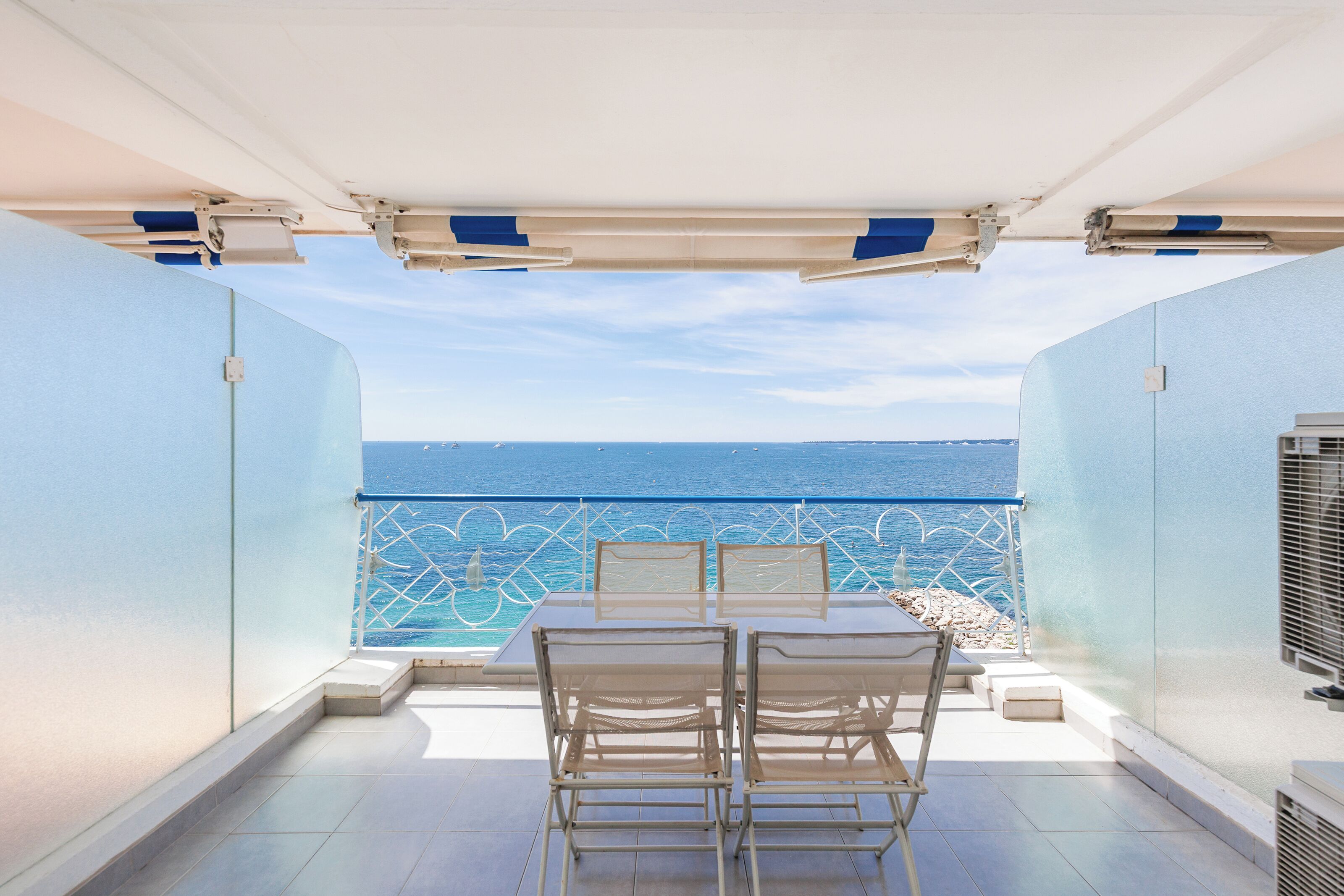 A terrace with a table and chairs, a railing, and a view of the sea.