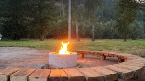 Un foyer en béton où brûle un feu, entouré d’un banc en bois servant de coin salon.