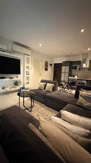 A modern living room with a sectional sofa, a flat-screen TV, and a kitchen in the background. - Fresh city premier homes  (Accra)