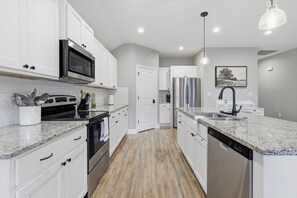A modern kitchen with white cabinets, stainless steel appliances, granite countertops, and a wooden floor. - 3 Bedroom Family House in Lake Charles, La (Lake Charles)