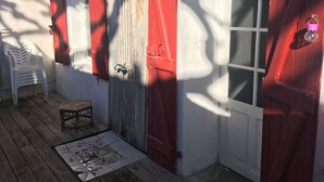 A wooden deck with a white plastic chair, a small table, and a tiled floor with a floral pattern. - Charming, super-central Landes house (Vieux-Boucau-les-Bains)