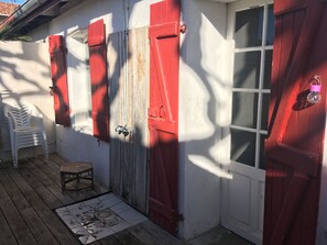 Eine Holzterrasse mit einem weißen Plastikstuhl, einem kleinen Tisch und einem gefliesten Boden mit floralem Muster.