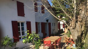A courtyard with a wooden table and chairs, potted plants, and a building with red shutters. - Charming, super-central Landes house (Vieux-Boucau-les-Bains)