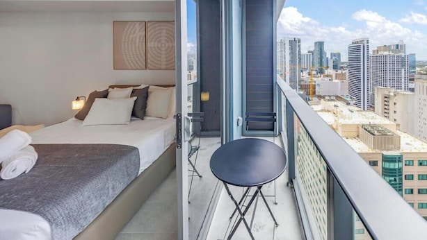 A hotel room with a bed, a small table, a balcony with a city view, and a window with a cityscape. - Cozy Skyline Condo - Cityview Miami (Miami)