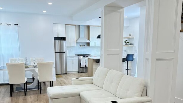 Een moderne woonkamer met een hoekbank, een eethoek met stoelen en een keuken op de achtergrond.