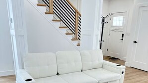 Een witte hoekbank in een kamer met houten vloeren en een trap met houten leuningen.