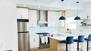 Een moderne keuken met witte kasten, roestvrijstalen apparatuur en een centraal eiland met barstoelen.