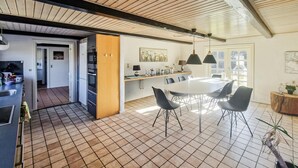 Une cuisine moderne avec un coin repas, comprenant un grand îlot central, des luminaires suspendus et une vue sur l’extérieur.