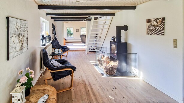 Une pièce spacieuse avec un plancher en bois, un fauteuil en cuir noir, une petite table sur laquelle est posée une lanterne et une cheminée.