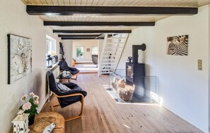 Une pièce spacieuse avec un plancher en bois, un fauteuil en cuir noir, une petite table sur laquelle est posée une lanterne et une cheminée.