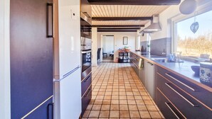 Une cuisine moderne avec un carrelage au sol, des meubles de couleur sombre et une fenêtre donnant sur un jardin.