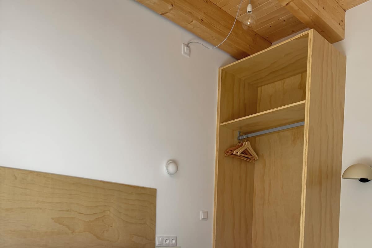 Un dormitorio con cabecera de madera, cama con ropa de cama blanca, armario de madera, mesita de noche y lámpara colgante.