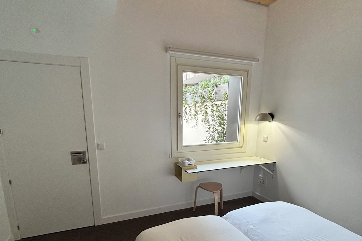 Un dormitorio con una cama, un escritorio con una silla, una ventana y una lámpara en el techo.