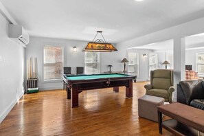 A pool table in a room with wooden floors, a green cushioned bench, and a hanging light fixture.