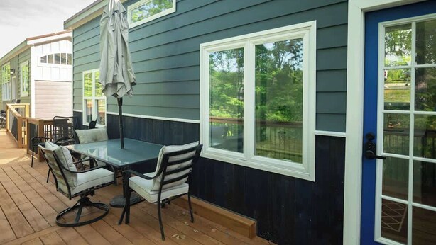 Une terrasse extérieure couverte, avec une table et des chaises, une porte bleue et une fenêtre donnant sur une courClose.