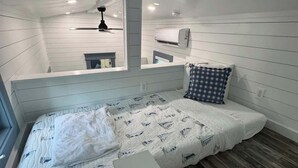 Une chambre compacte avec un lit simple, un plafond en pente, un ventilateur de plafond, un appareil de climatisation et une fenêtre.