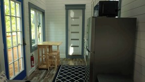 Une cuisine de taille réduite, avec une table en bois, un réfrigérateur et une porte donnant sur un balcon.
