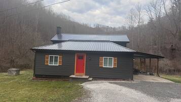 A small, single-story cabin with a red door, two windows with shutters, and a metal roof.