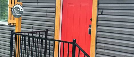 Un bâtiment avec une porte rouge, une boîte aux lettres et une pancarte indiquant « Bienvenue ».