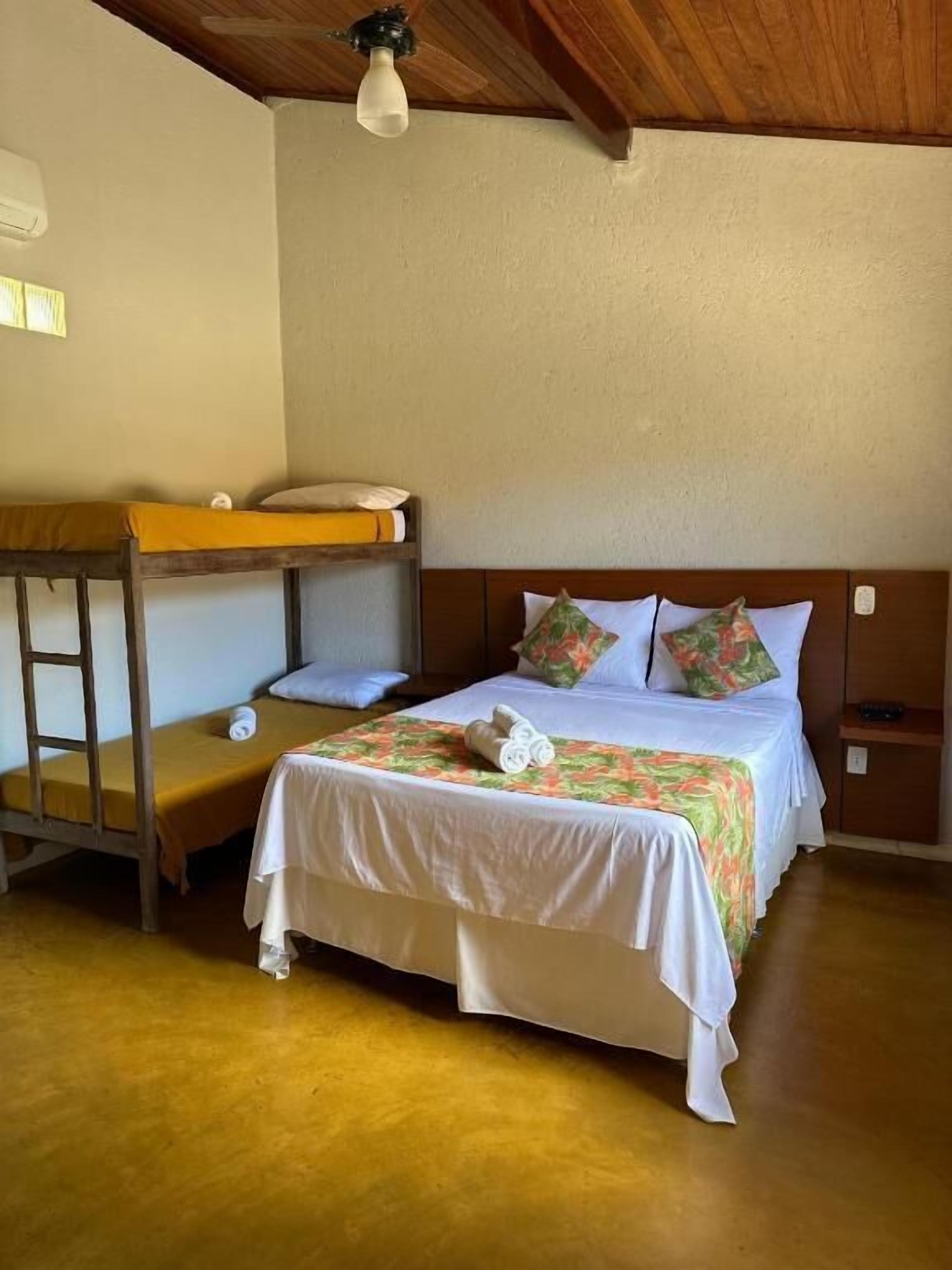 Una cama individual con cubrecama floral, una cama nido de madera y una mesita de noche con lámpara.