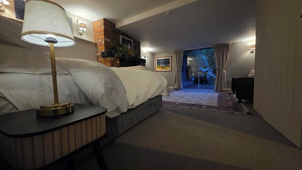 Une chambre à coucher avec un lit, une lampe de chevet et une vue sur un jardin, visible à travers une porte vitrée.