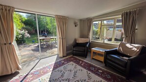Un salon comprenant un canapé, un fauteuil, une petite table, un tapis et une porte-fenêtre coulissante donnant sur une terrasse extérieure.
