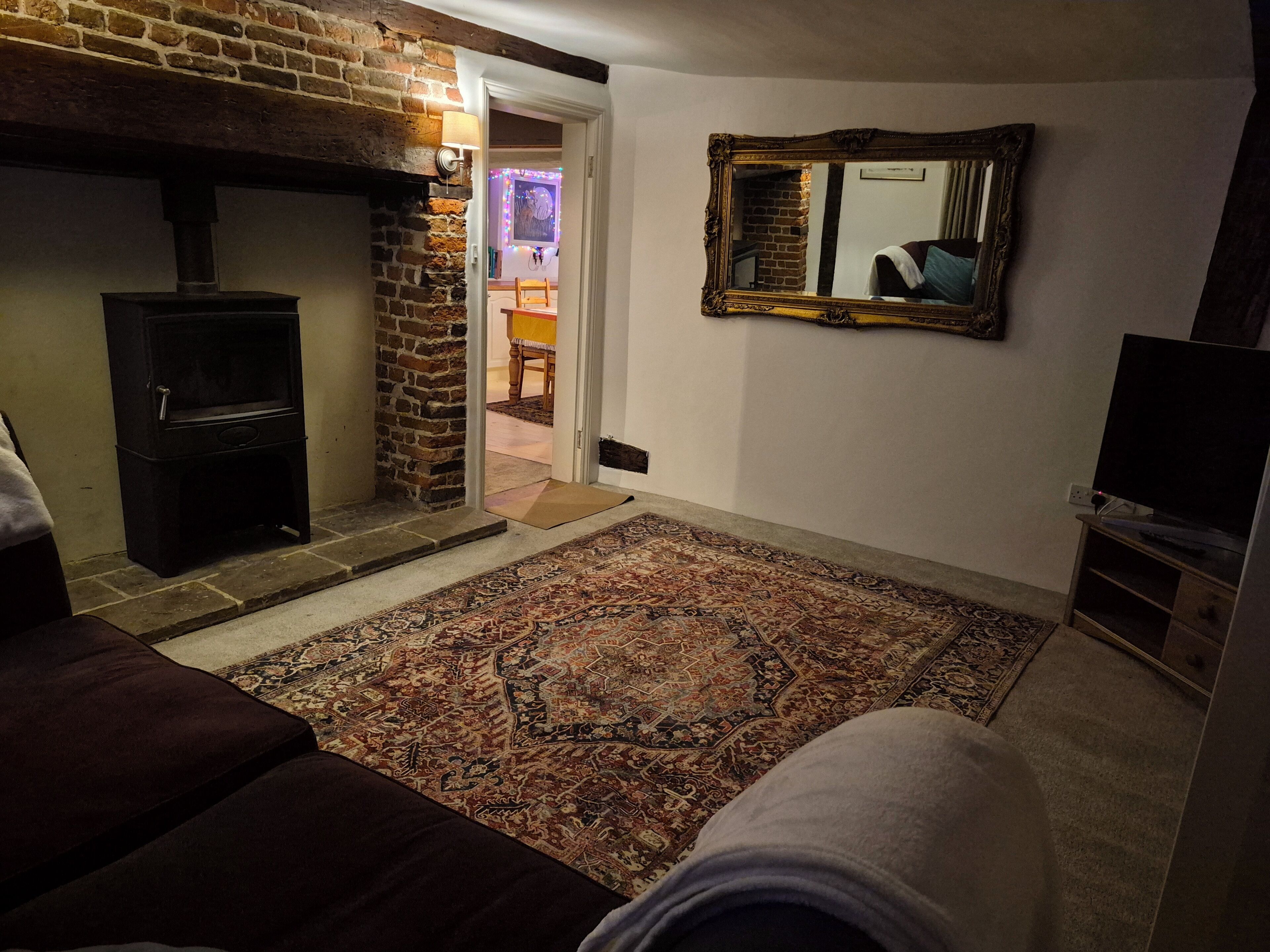 A cozy living room with a fireplace, a patterned rug, a television, and a mirror on the wall.